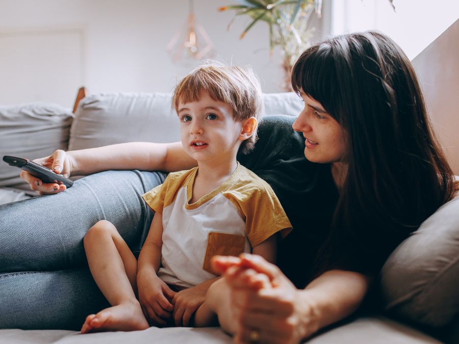 A young child and their mom cuddling on the couch watching TV.