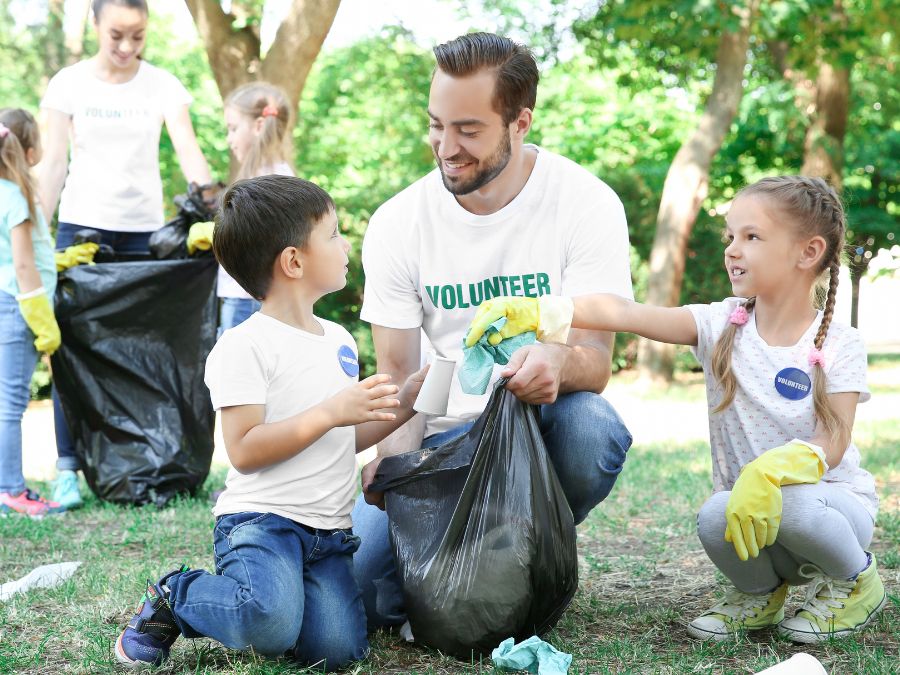 Two children and an adult wearing volunteer shirts, picking up trash in a park.