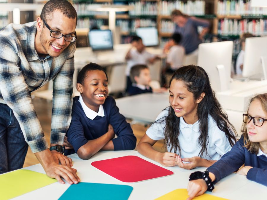 Teacher helping students at table with colorful folders.